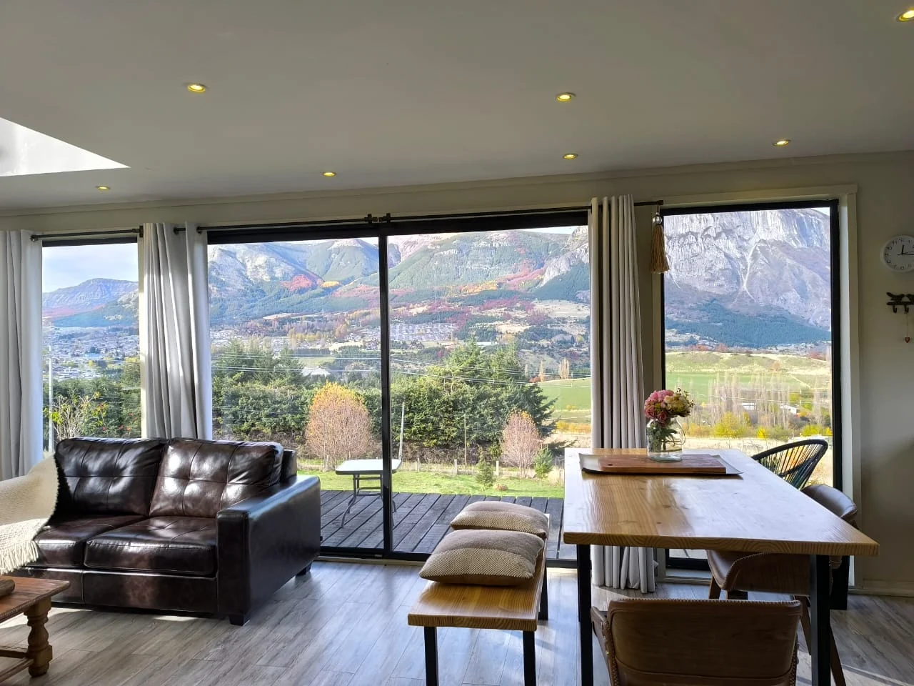Living de Casa Lavanda con sillón de cuero y comedor frente al ventanal con vista a los cerros de Coyhaique