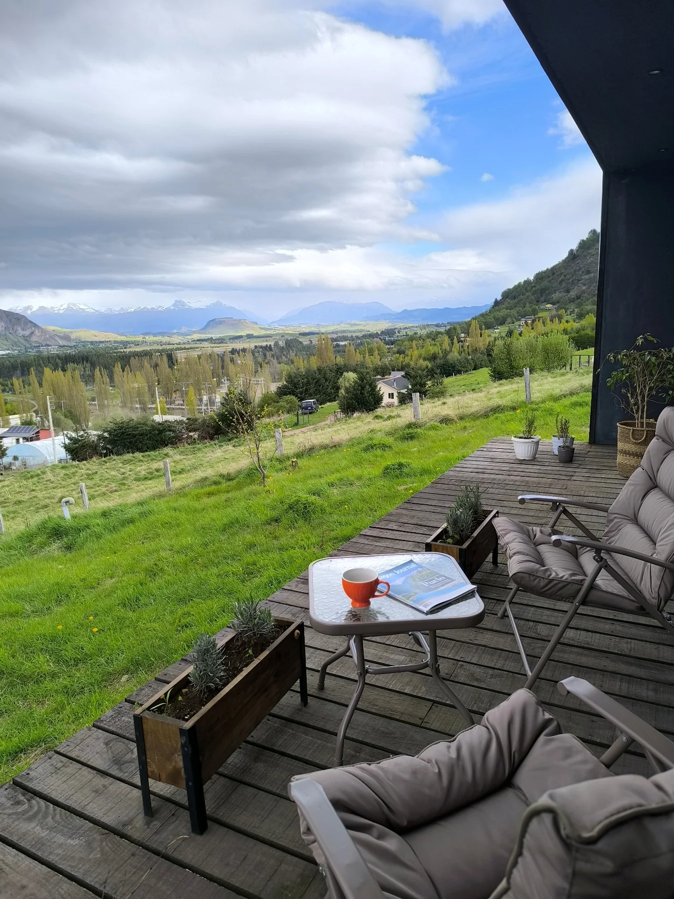 Terraza de madera con sillones y mesa frente al patio y los cerros